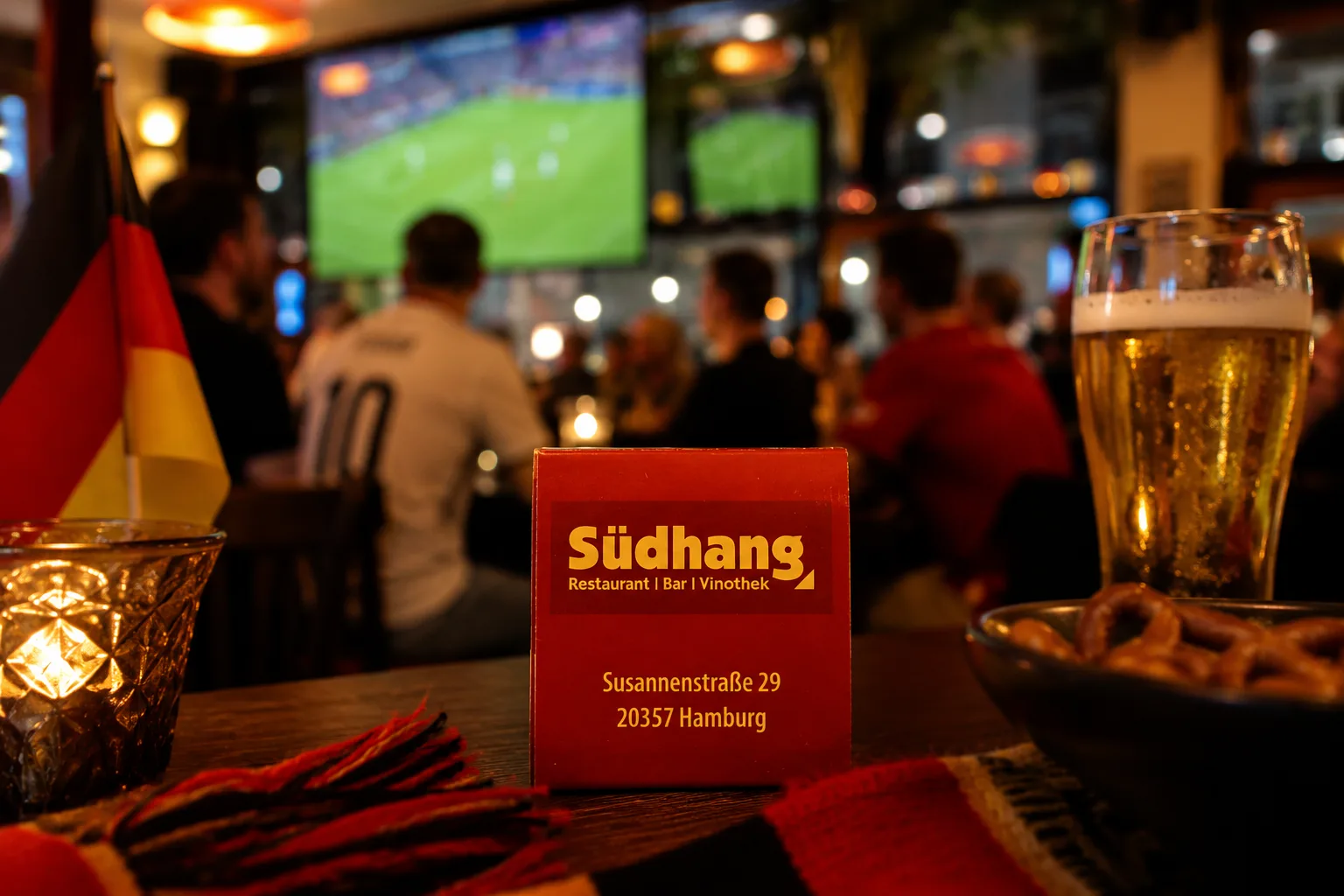 Südhang Logo auf einem Tisch mit Snacks, Bier, Deutschland-Schal und Fußballscreen im Hintergrund